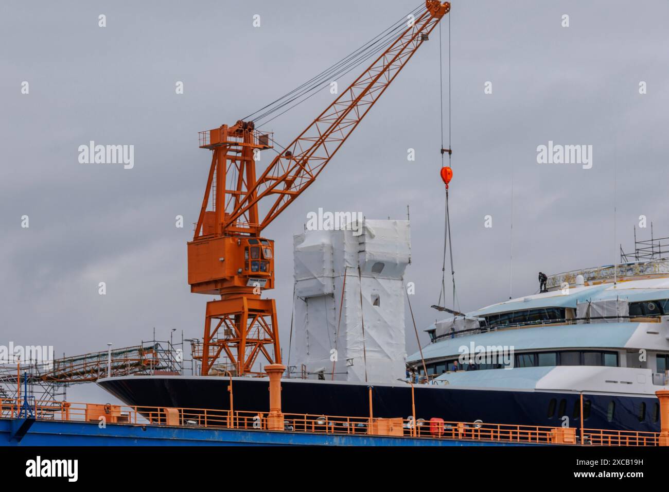 Una grande nave giace nel cantiere navale, fiancheggiata da una gru in arancione, Bremerhaven, Brema, Germania Foto Stock