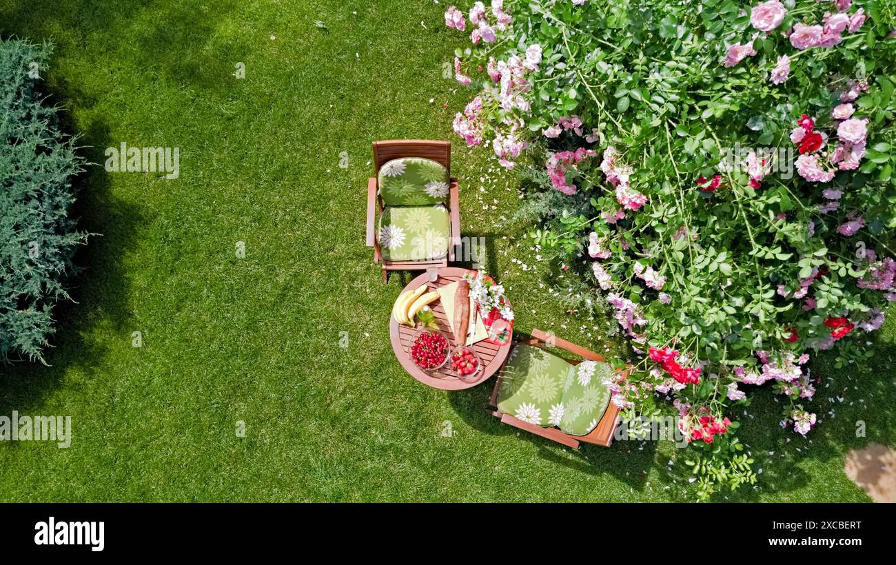 Tavolo decorato con pane, fragole e frutta nello splendido giardino di rose estivo, vista dall'alto del romantico tavolo da pranzo per due Foto Stock