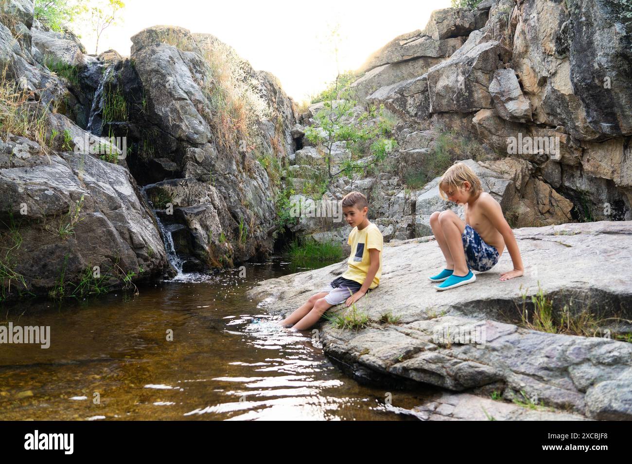 Due bambini seduti tranquillamente sulla riva di un fiume in natura Foto Stock