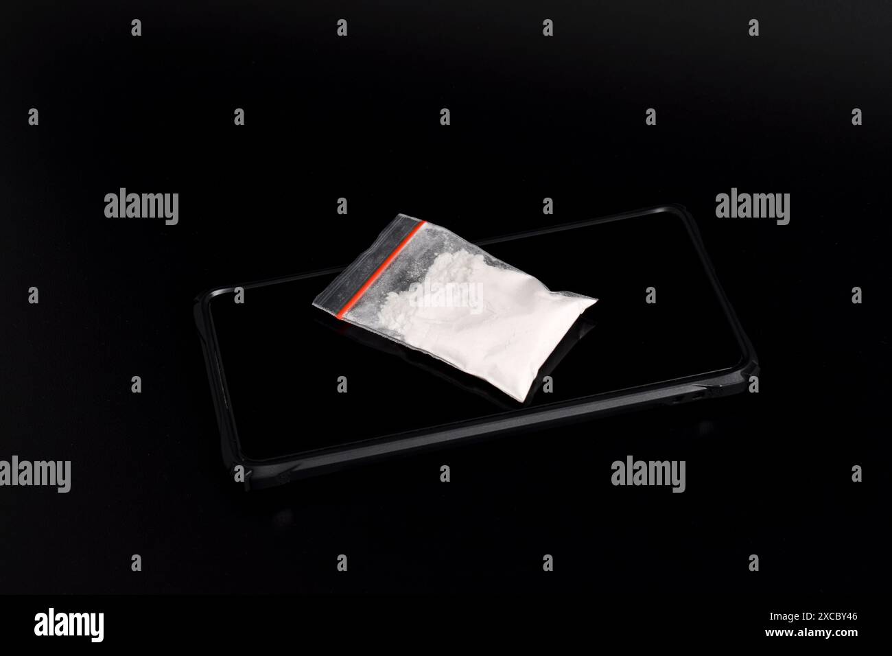 Cocaina in una confezione di plastica su uno smartphone isolato su sfondo nero. Illustrazione di sostanze stupefacenti illegali, narcotici Foto Stock