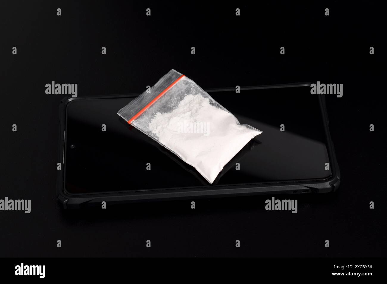Cocaina in una confezione di plastica su uno smartphone isolato su sfondo nero. Illustrazione di sostanze stupefacenti illegali, narcotici Foto Stock