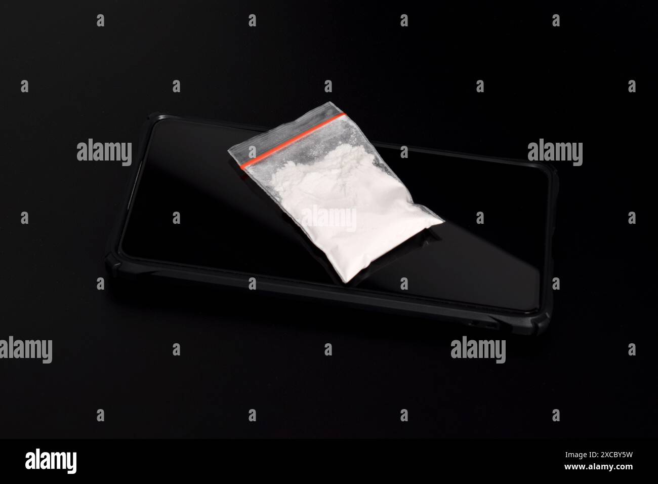 Cocaina in una confezione di plastica su uno smartphone isolato su sfondo nero. Illustrazione di sostanze stupefacenti illegali, narcotici Foto Stock