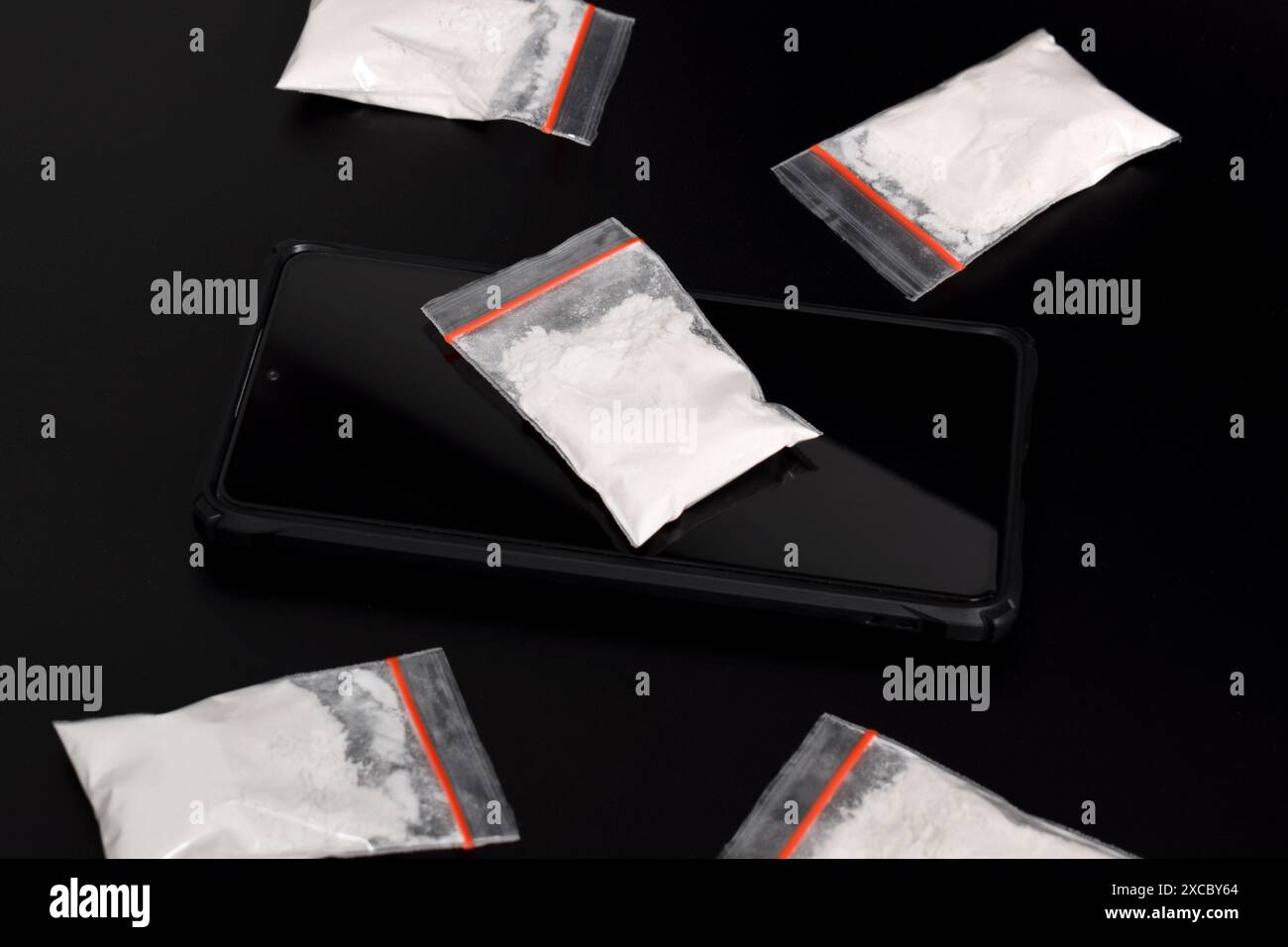 Cocaina in una confezione di plastica su uno smartphone isolato su sfondo nero. Illustrazione di sostanze stupefacenti illegali, narcotici Foto Stock