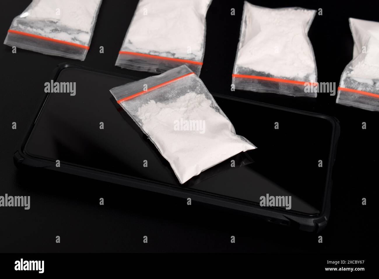 Cocaina in una confezione di plastica su uno smartphone isolato su sfondo nero. Illustrazione di sostanze stupefacenti illegali, narcotici Foto Stock