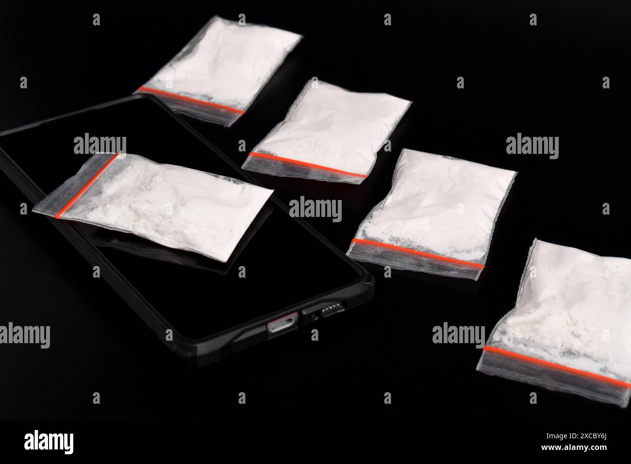 Cocaina in una confezione di plastica su uno smartphone isolato su sfondo nero. Illustrazione di sostanze stupefacenti illegali, narcotici Foto Stock