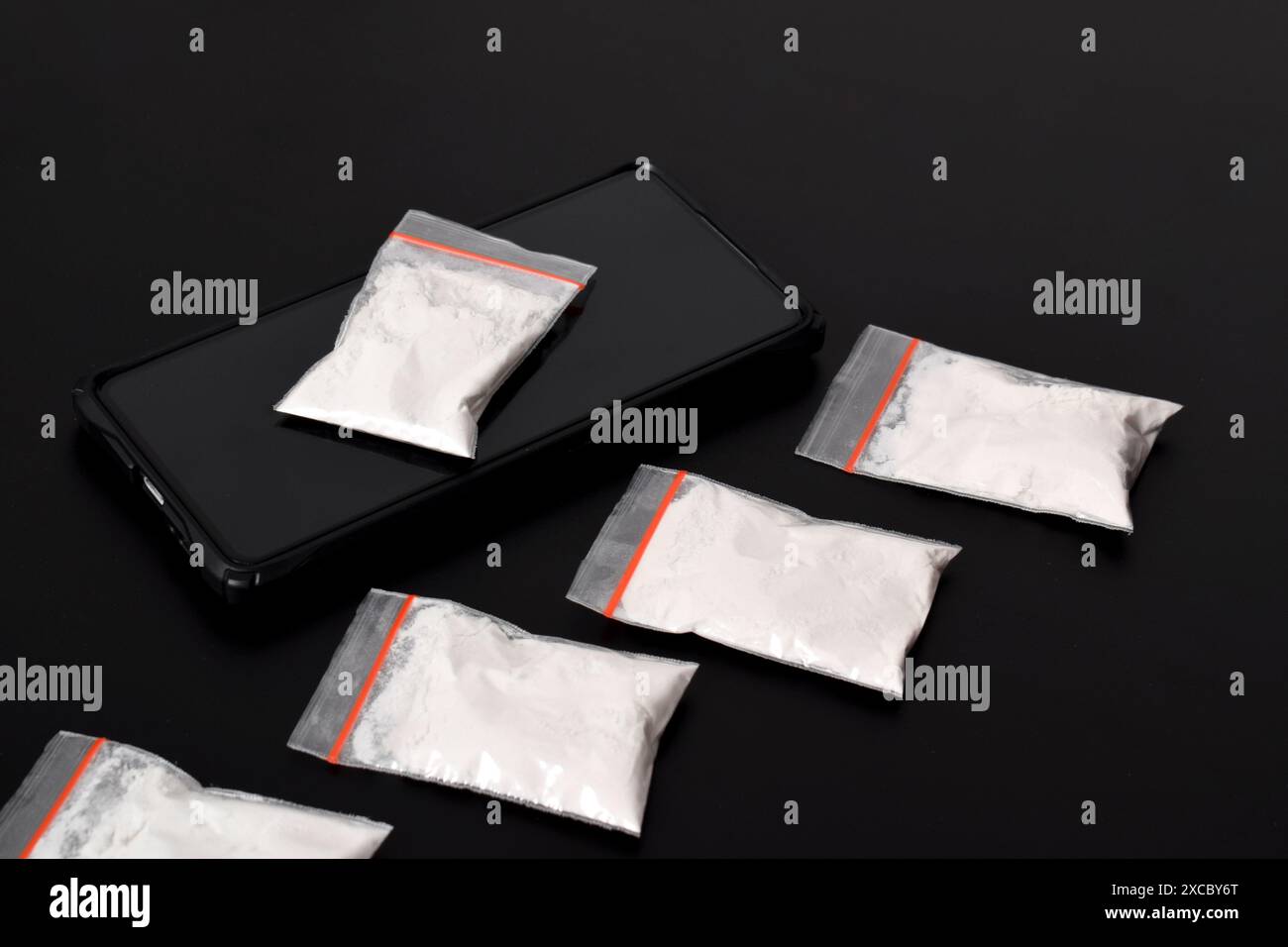 Cocaina in una confezione di plastica su uno smartphone isolato su sfondo nero. Illustrazione di sostanze stupefacenti illegali, narcotici Foto Stock