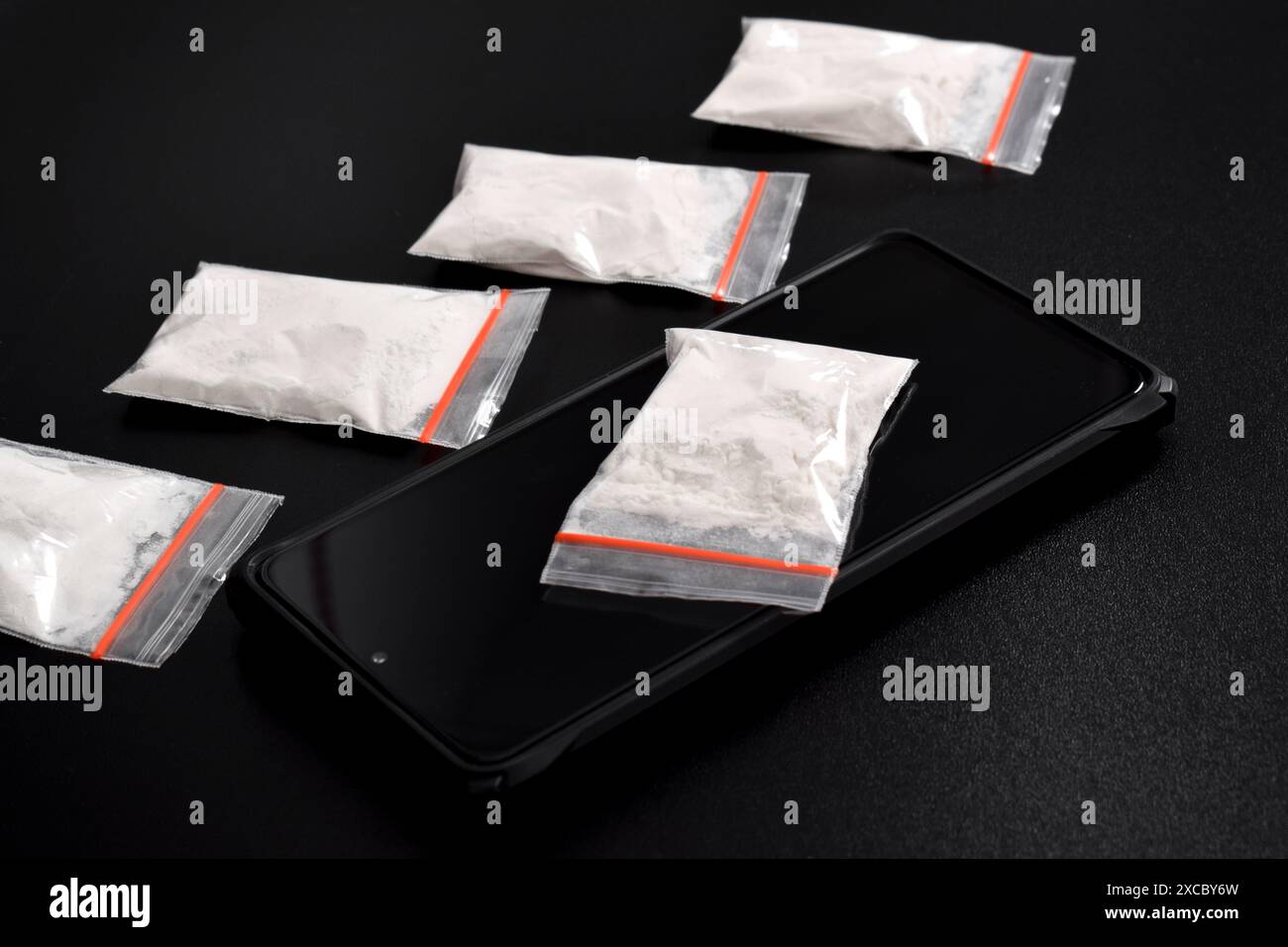 Cocaina in una confezione di plastica su uno smartphone isolato su sfondo nero. Illustrazione di sostanze stupefacenti illegali, narcotici Foto Stock