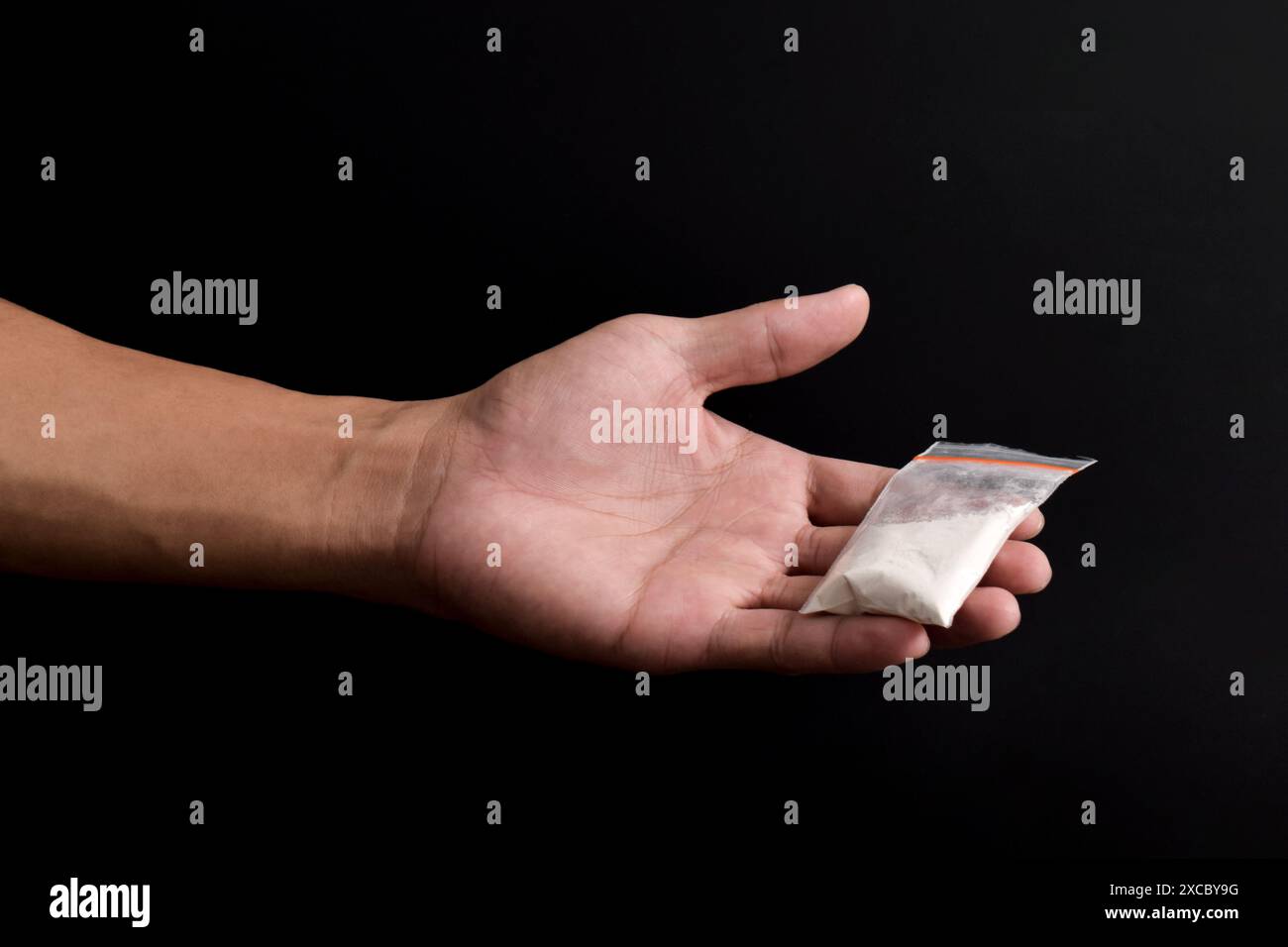 Mano che tiene la cocaina in un pacchetto di plastica isolato su sfondo nero. illustrazione di sostanze stupefacenti illegali, narcotici Foto Stock