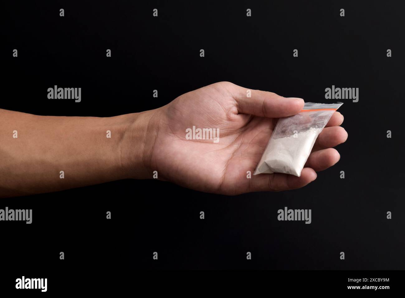 Cocaina a mano in un contenitore di plastica isolato su sfondo nero. Illustrazione di sostanze stupefacenti illegali, narcotici Foto Stock