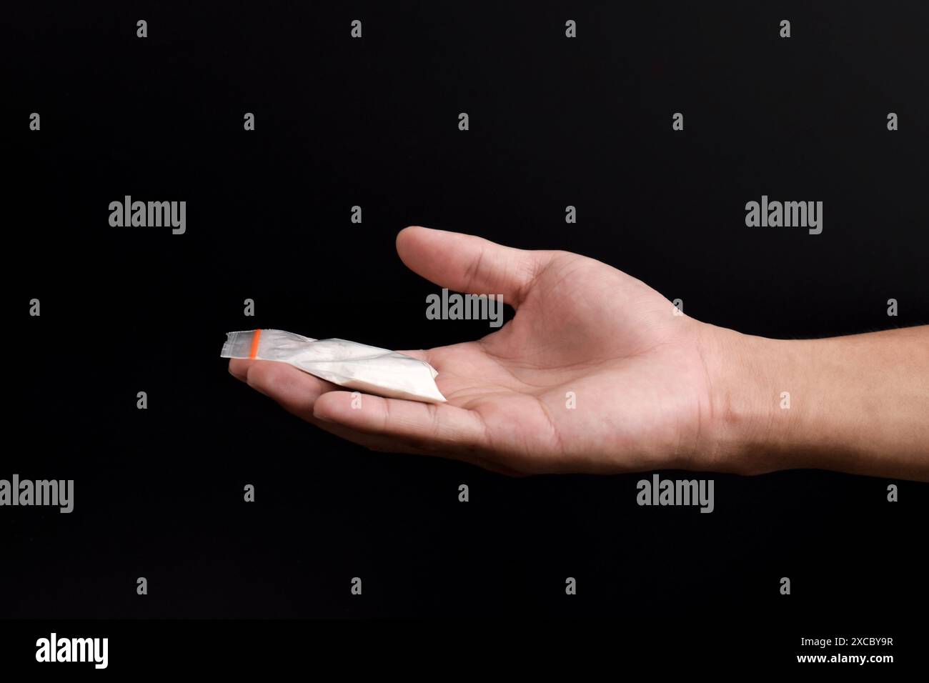 Mano che tiene la cocaina in un pacchetto di plastica isolato su sfondo nero. illustrazione di sostanze stupefacenti illegali, narcotici Foto Stock