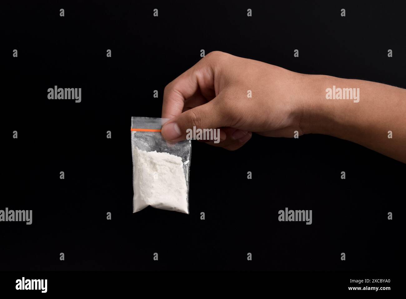 Mano che tiene la cocaina in un pacchetto di plastica isolato su sfondo nero. illustrazione di sostanze stupefacenti illegali, narcotici Foto Stock