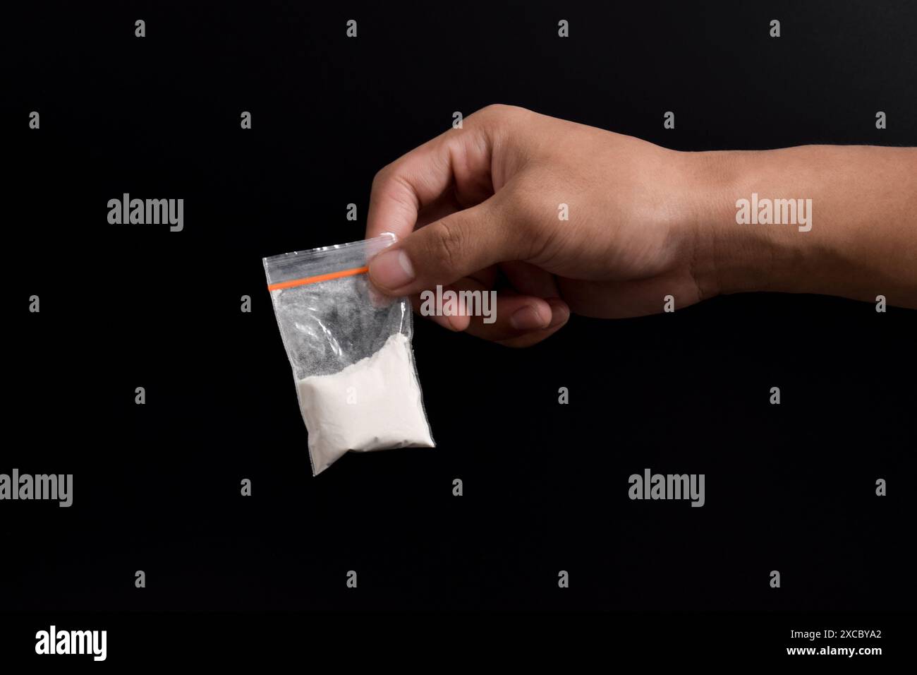 Cocaina a mano in un contenitore di plastica isolato su sfondo nero. Illustrazione di sostanze stupefacenti illegali, narcotici Foto Stock
