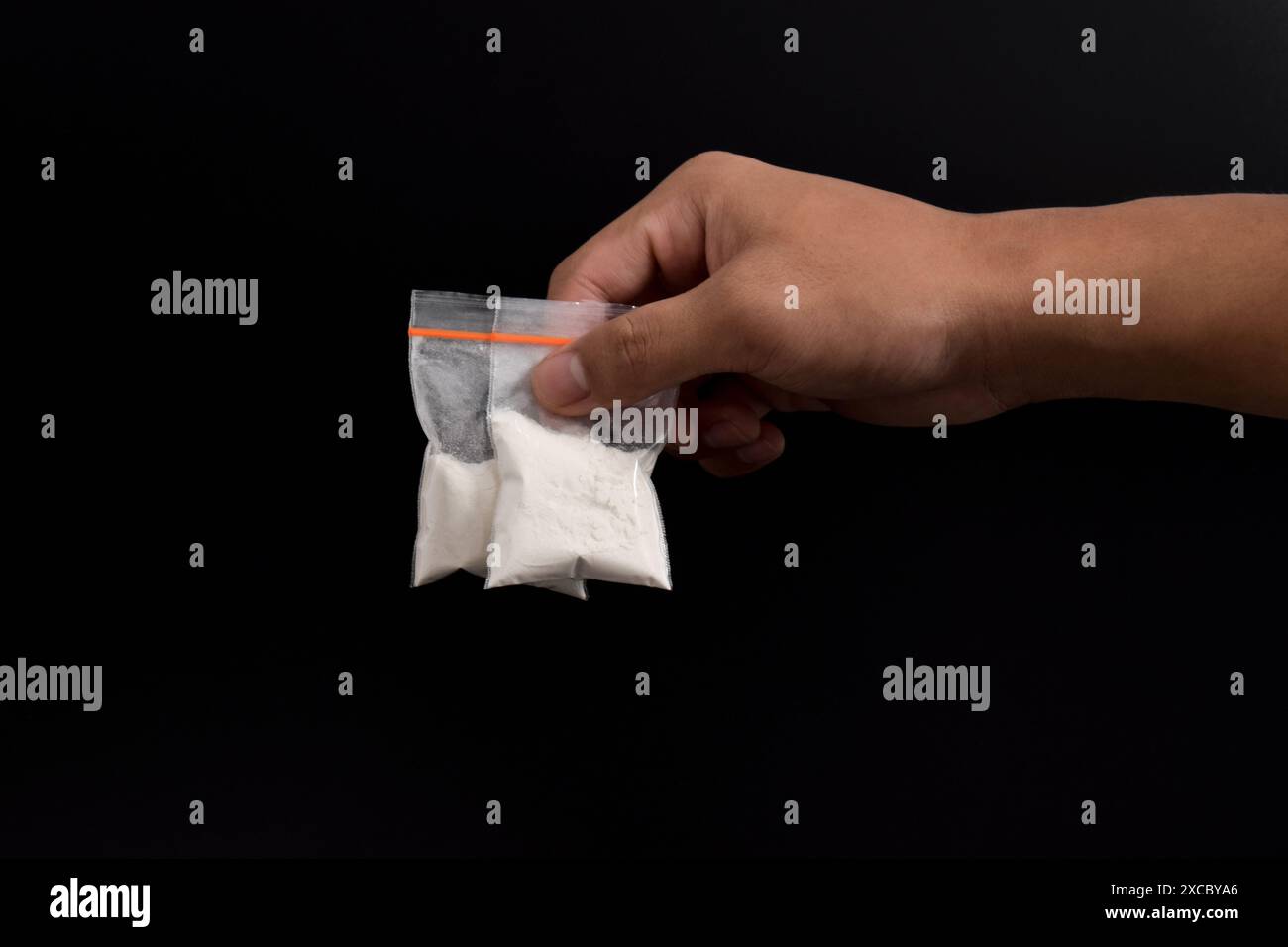 Mano che tiene la cocaina in un pacchetto di plastica isolato su sfondo nero. illustrazione di sostanze stupefacenti illegali, narcotici Foto Stock