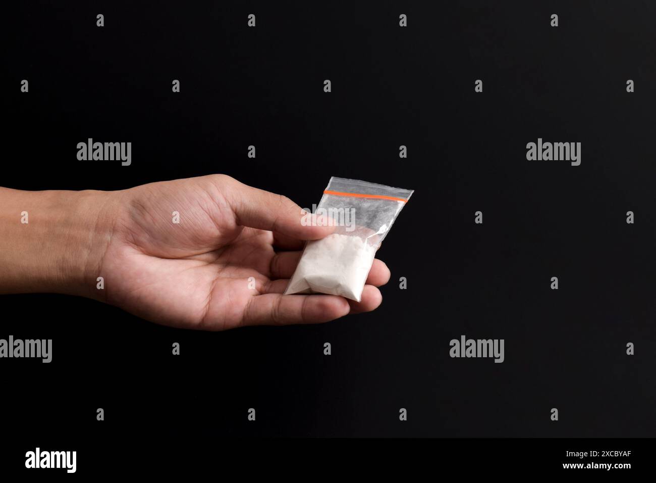 Cocaina a mano in un contenitore di plastica isolato su sfondo nero. Illustrazione di sostanze stupefacenti illegali, narcotici Foto Stock