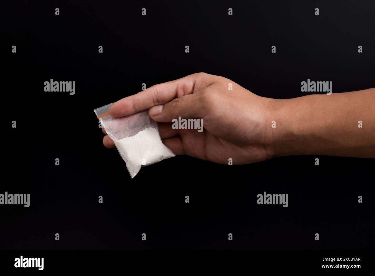 Mano che tiene la cocaina in un pacchetto di plastica isolato su sfondo nero. illustrazione di sostanze stupefacenti illegali, narcotici Foto Stock