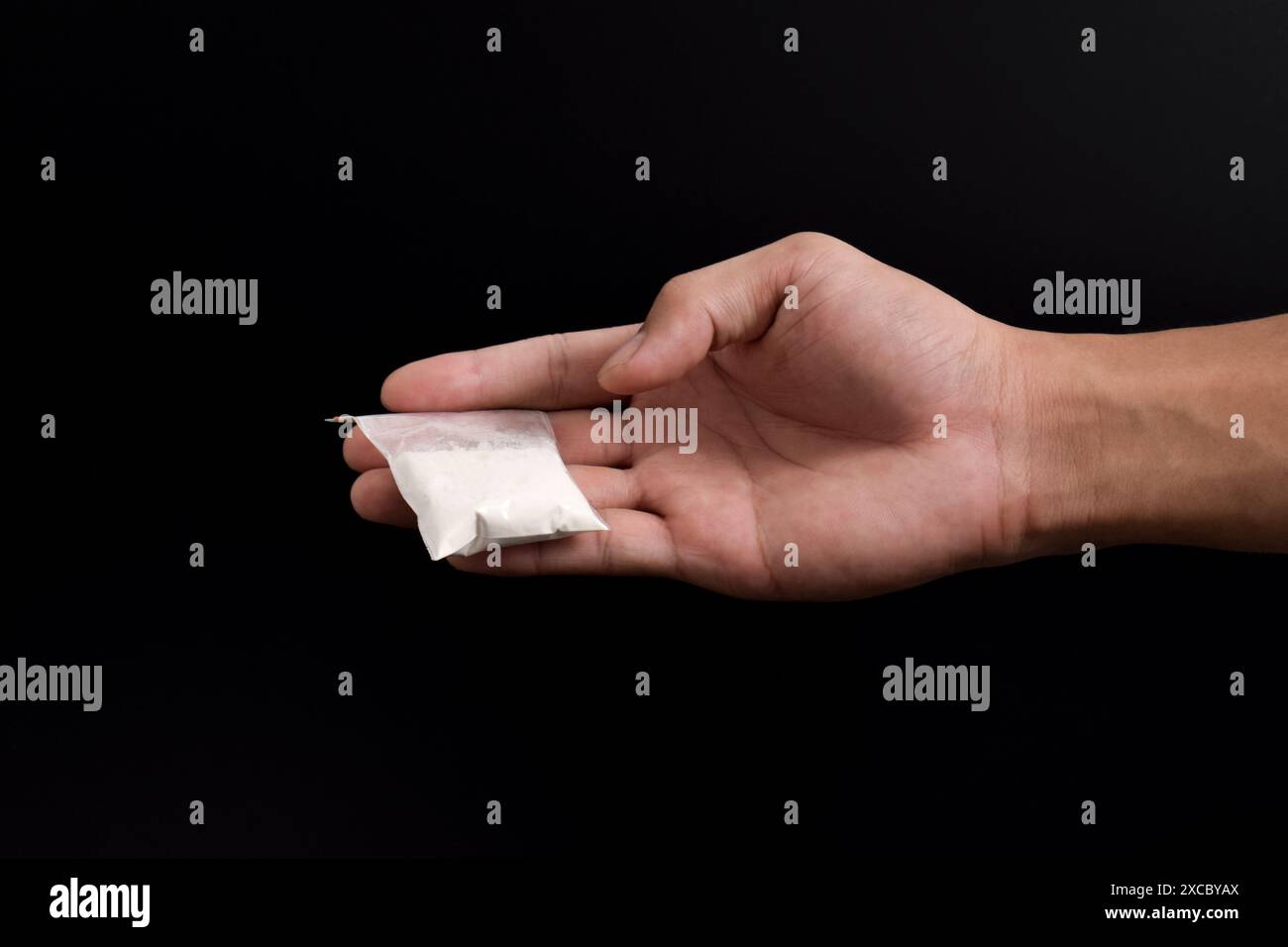 Cocaina a mano in un contenitore di plastica isolato su sfondo nero. Illustrazione di sostanze stupefacenti illegali, narcotici Foto Stock