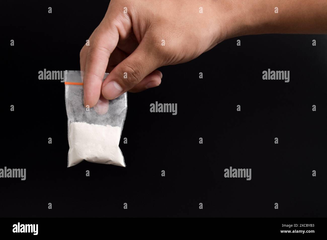 Mano che tiene la cocaina in un pacchetto di plastica isolato su sfondo nero. illustrazione di sostanze stupefacenti illegali, narcotici Foto Stock