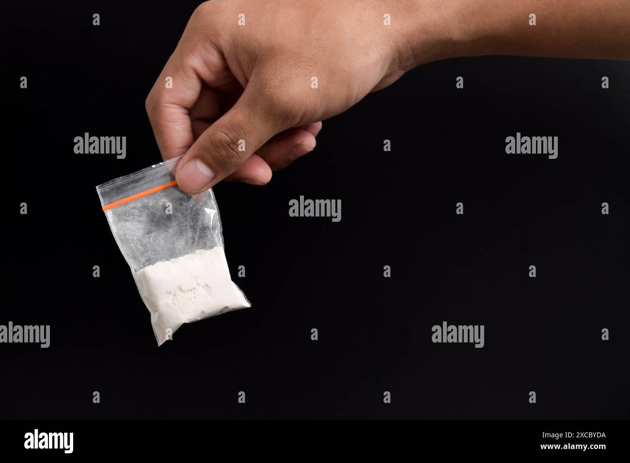 Mano che tiene la cocaina in un pacchetto di plastica isolato su sfondo nero. illustrazione di sostanze stupefacenti illegali, narcotici Foto Stock