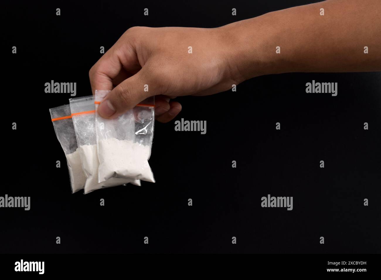 Cocaina a mano in un contenitore di plastica isolato su sfondo nero. Illustrazione di sostanze stupefacenti illegali, narcotici Foto Stock