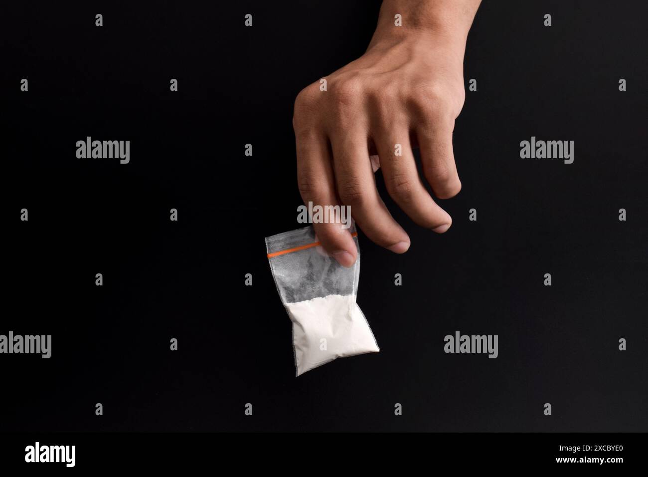 Mano che tiene la cocaina in un pacchetto di plastica isolato su sfondo nero. illustrazione di sostanze stupefacenti illegali, narcotici Foto Stock
