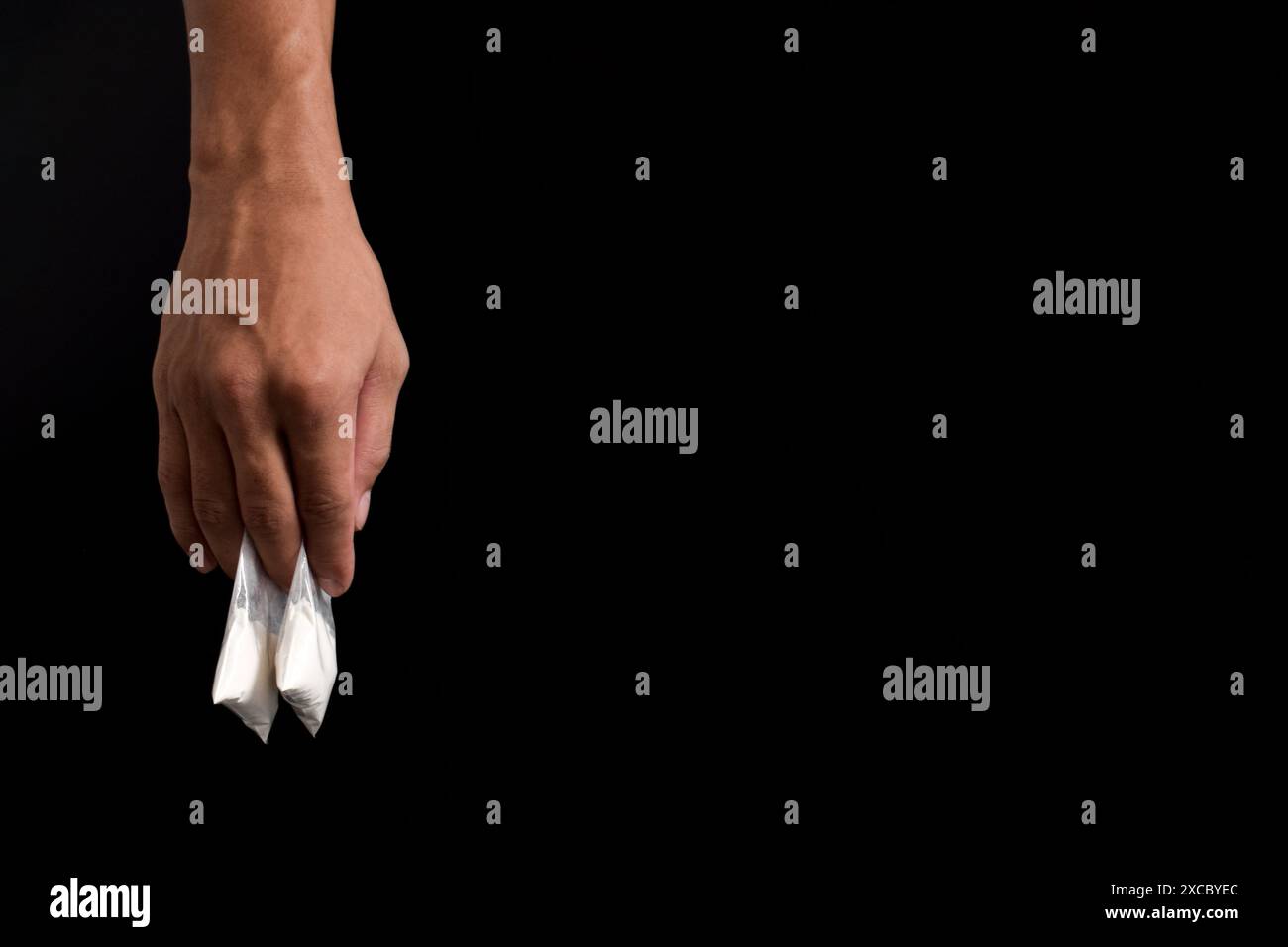 Mano che tiene la cocaina in un pacchetto di plastica isolato su sfondo nero. illustrazione di sostanze stupefacenti illegali, narcotici Foto Stock