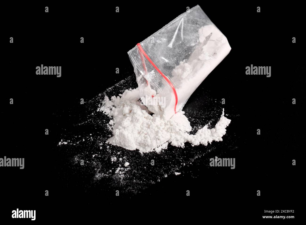Cocaina in confezione di plastica spolverata su sfondo nero. Illustrazione di sostanze stupefacenti illegali, narcotici Foto Stock