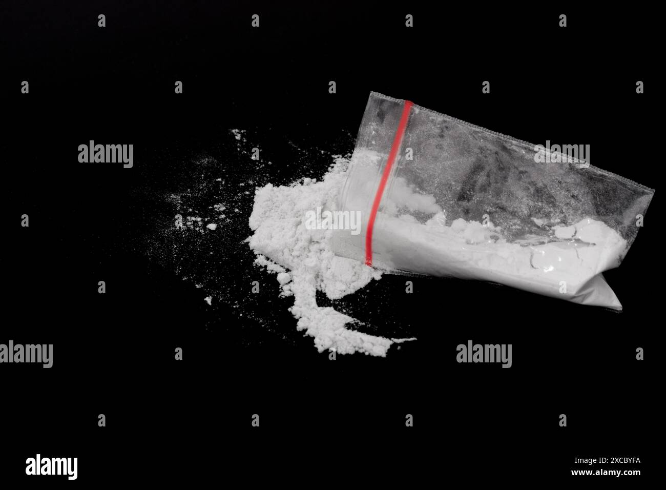 Cocaina in confezione di plastica spolverata su sfondo nero. Illustrazione di sostanze stupefacenti illegali, narcotici Foto Stock