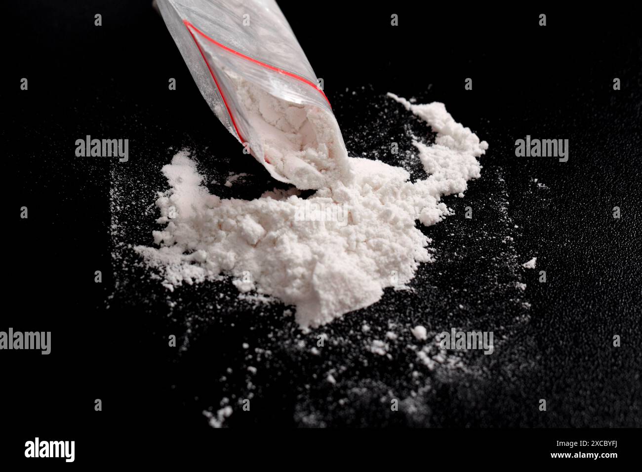 Cocaina in confezione di plastica spolverata su sfondo nero. Illustrazione di sostanze stupefacenti illegali, narcotici Foto Stock