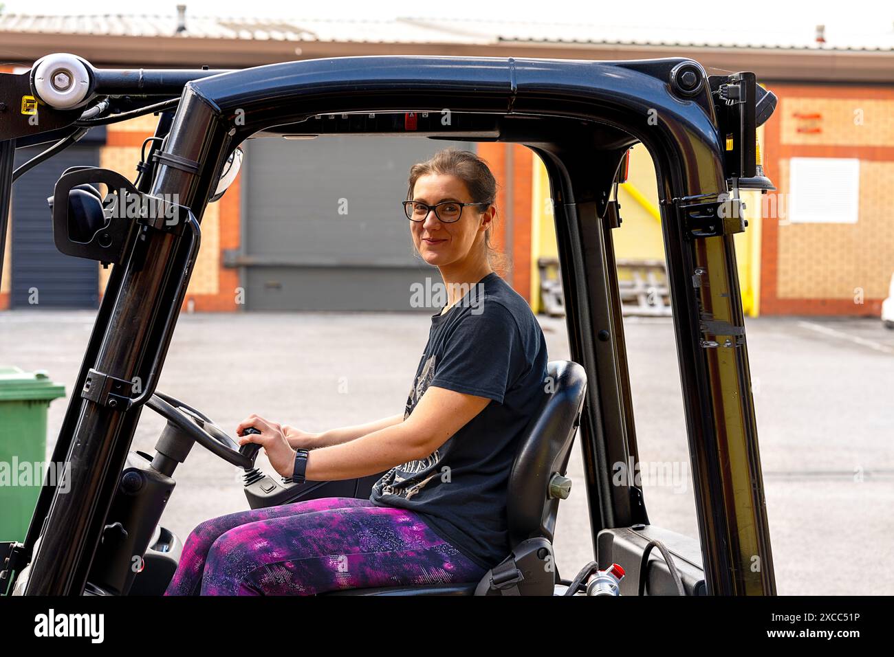 Giovane donna sorridente 20-30 che gestisce un carrello elevatore in un ambiente di lavoro industriale. Foto Stock