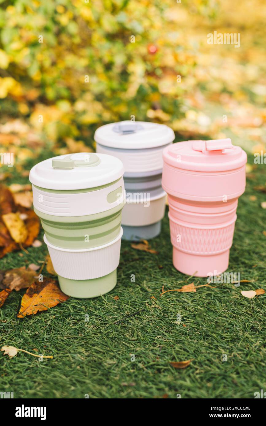 Tazze pieghevoli ecologiche o tazze pieghevoli in silicone con erba verde e foglie cadute sullo sfondo autunnale Foto Stock