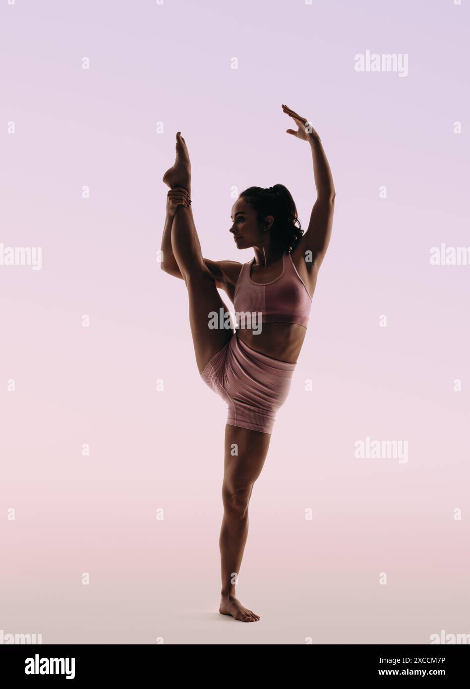 Donna che mostra una notevole abilità nella ginnastica mentre si trova in piedi su uno sfondo da studio. Foto Stock