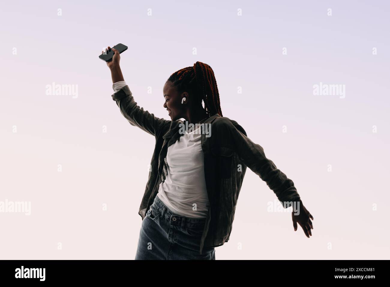 La giovane donna felice balla espressivamente in uno studio. Con gli auricolari, si sposta verso la musica, festeggiando e divertendosi. Il suo sorriso irradia gioia. Foto Stock