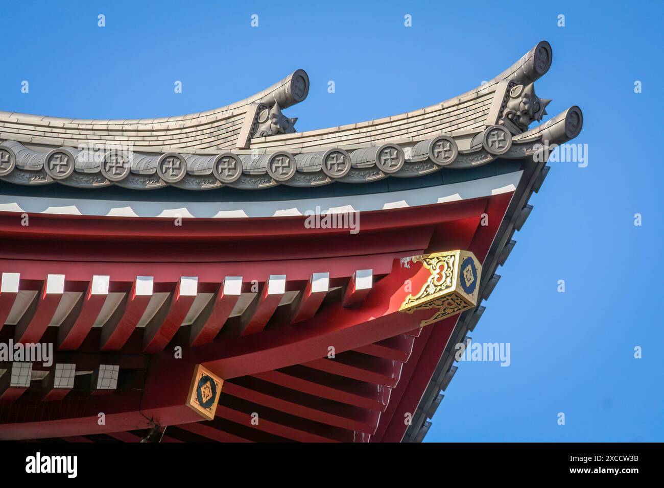 Primo piano di un tetto a pagoda con travi rosse, accenti bianchi e dorati e coperture grigie riccamente ornate sul tetto del tempio buddista senso-ji e delle Fiv Foto Stock