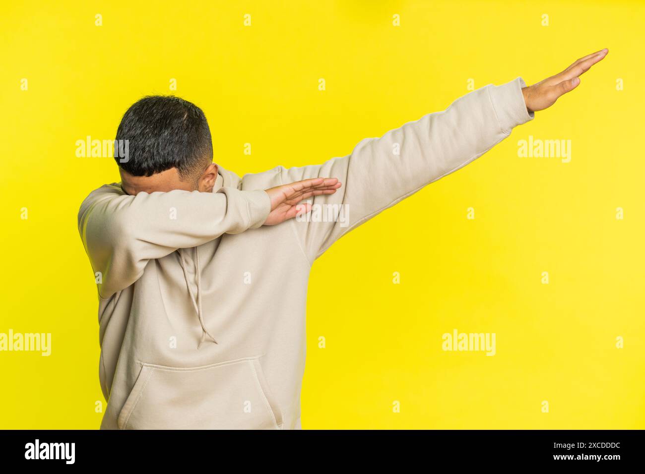 Uomo indiano positivo e alla moda che si diverte a ballare e a muoversi al ritmo, alzando le mani, facendo vincere il dub dance celebrando il gesto della vittoria. Felice ragazzo arabo isolato su sfondo giallo Foto Stock