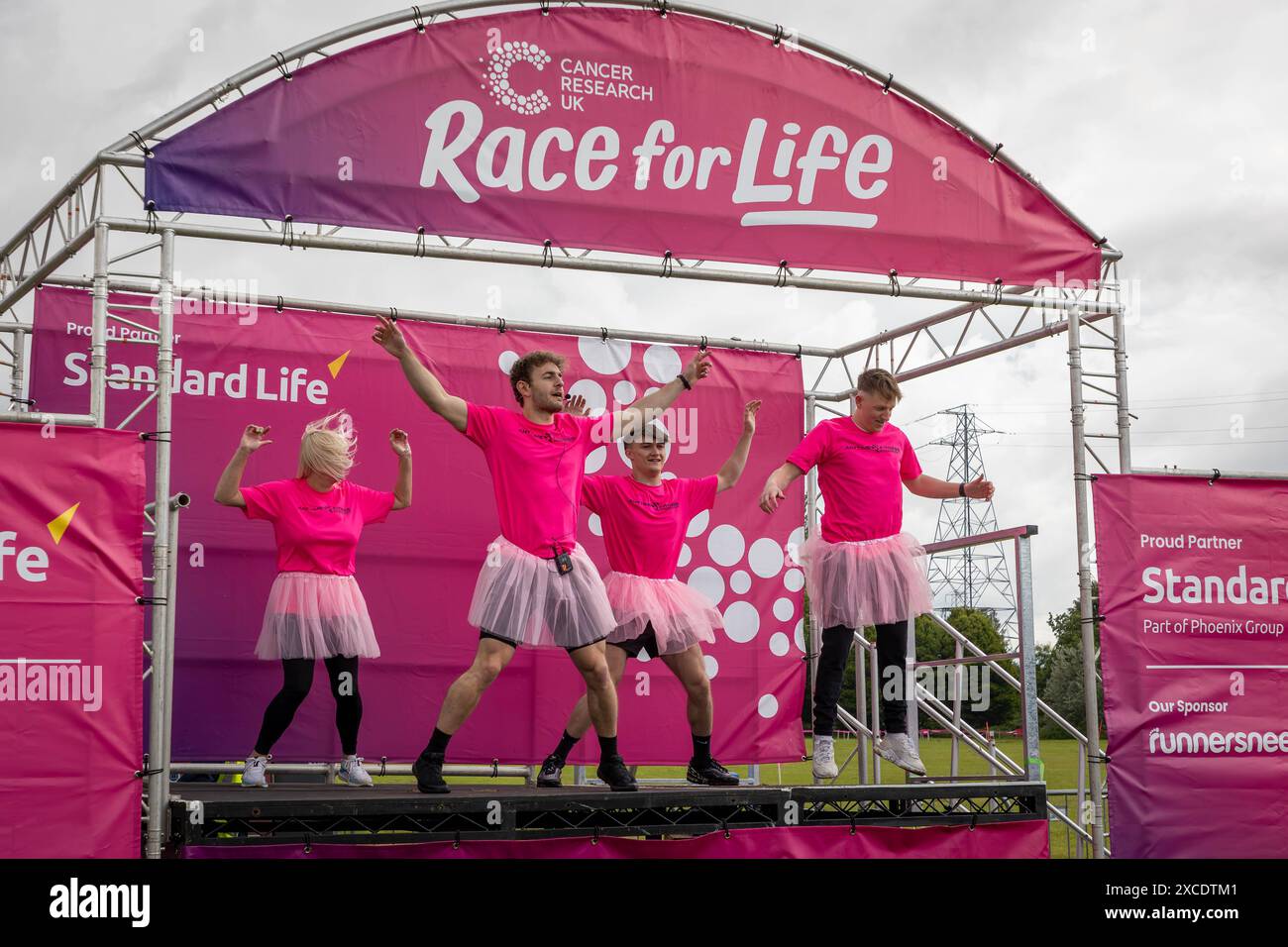 Warrington, Cheshire, Regno Unito. 16 giugno 2024. La "Race for Life" annuale a sostegno della Cancer Research UK si è svolta a Victoria Park, Warrington. Gli istruttori della palestra locale hanno istruito i corridori a riscaldarsi prima della gara crediti: John Hopkins/Alamy Live News Foto Stock