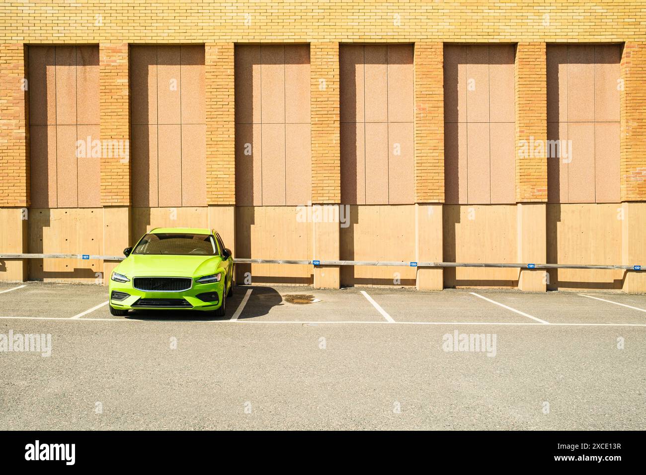 Un'auto verde calce è parcheggiata in un parcheggio. L'auto è rivolta verso la telecamera ed è parcheggiata di fronte a un muro di mattoni. Il muro ha sei colonne di cemento Foto Stock