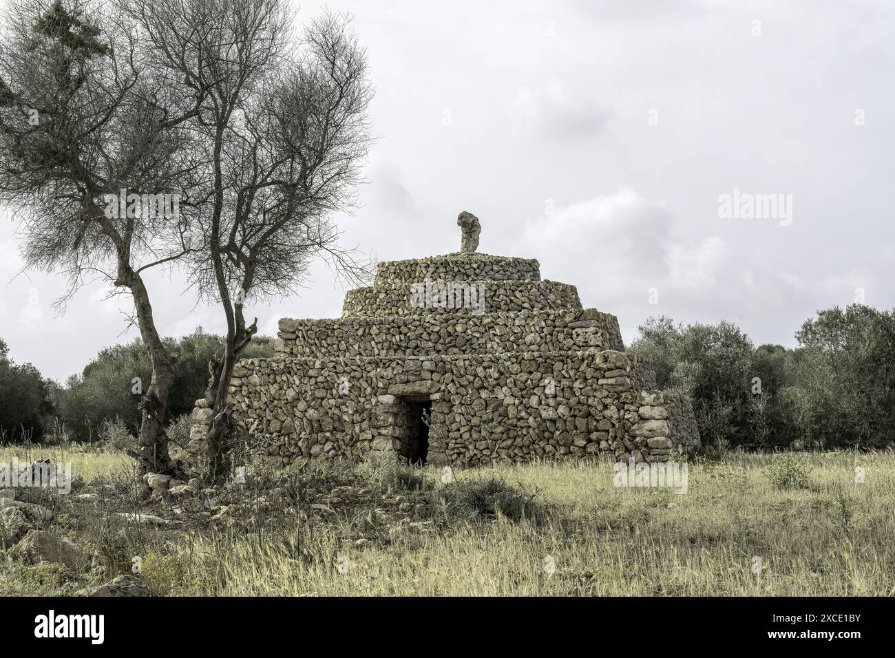 Una tradizionale struttura in pietra secca a Minorca, caratterizzata da un design a gradini con ingresso. La struttura si trova in un campo rurale, sotto una parte nuvolosa Foto Stock