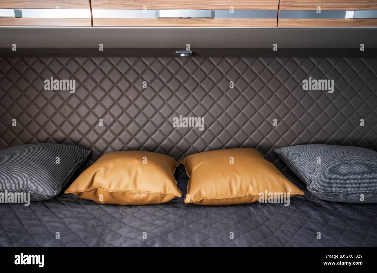 Un primo piano di un letto in un moderno camper. Il letto è realizzato con biancheria grigio scuro e dispone di tre cuscini. Due cuscini sono di colore marrone Foto Stock