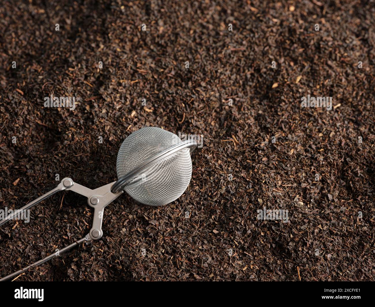 L'infusore di tè in metallo si trova su foglie di tè nero secco, pronto per essere utilizzato per una tazza perfetta di tè Foto Stock