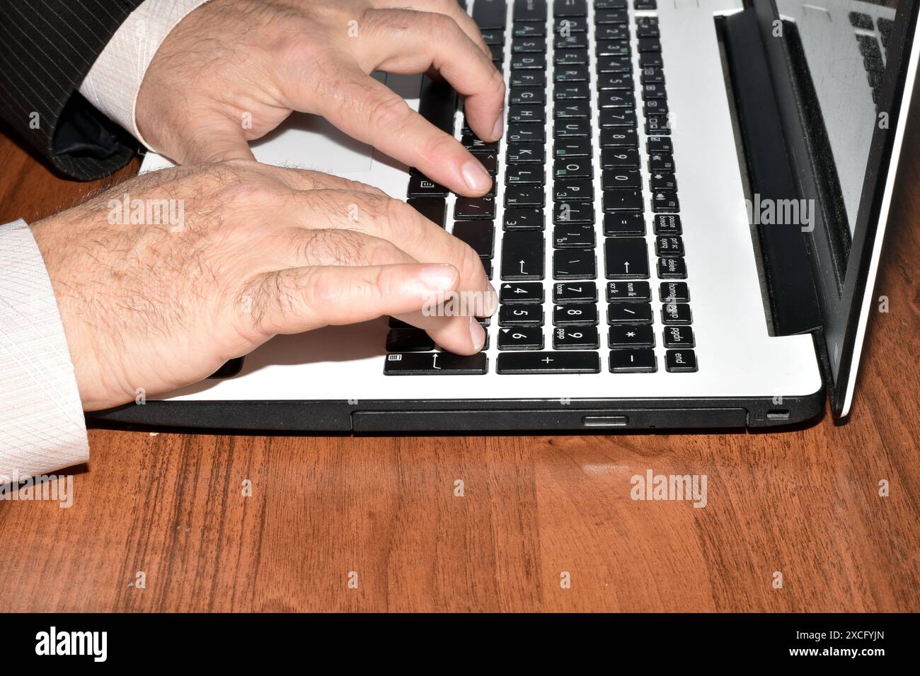L'immagine mostra le mani di un uomo seduto a un tavolo e che lavora su un notebook. Foto Stock