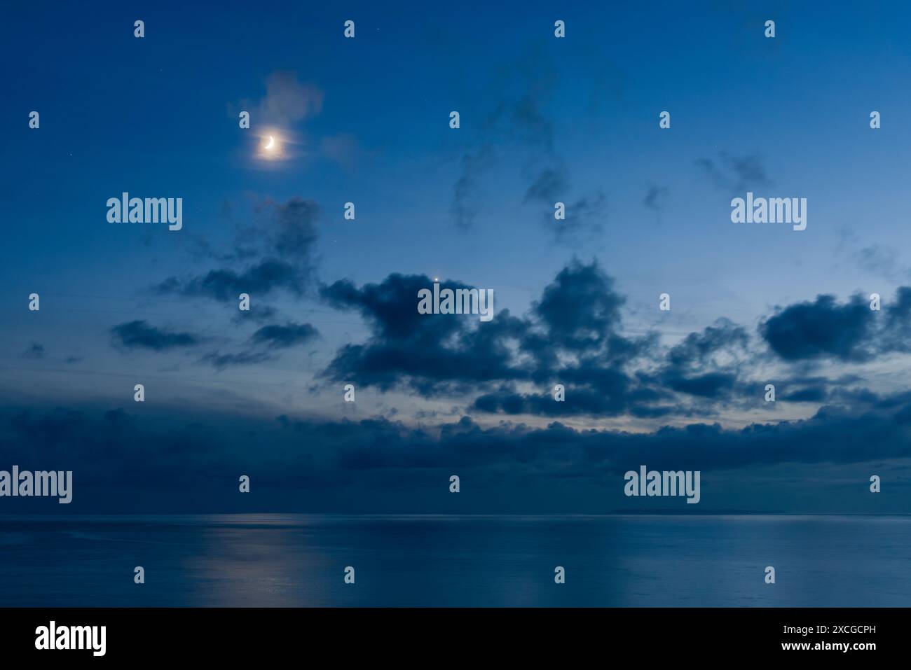 Una luna crescente e il pianeta Venere in un cielo crepuscolo sopra l'Oceano Atlantico settentrionale e Lundy Island vista da Westward ho!, Devon, Inghilterra. Foto Stock