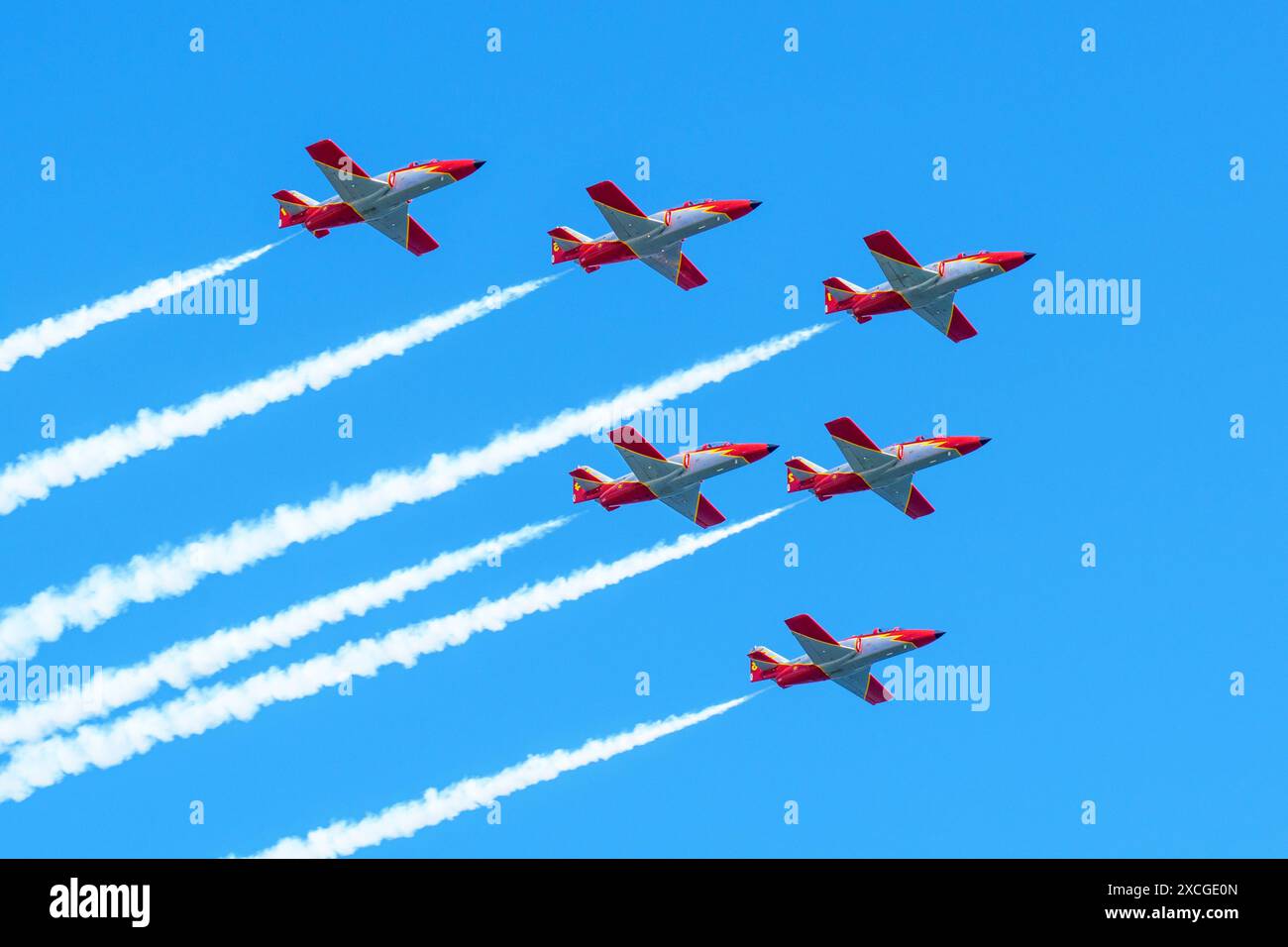 Gijon, Spagna - 24 maggio 2024: Sei caccia a reazione rossi e bianchi volano in formazione, lasciando tracce di fumo contro un cielo azzurro Foto Stock