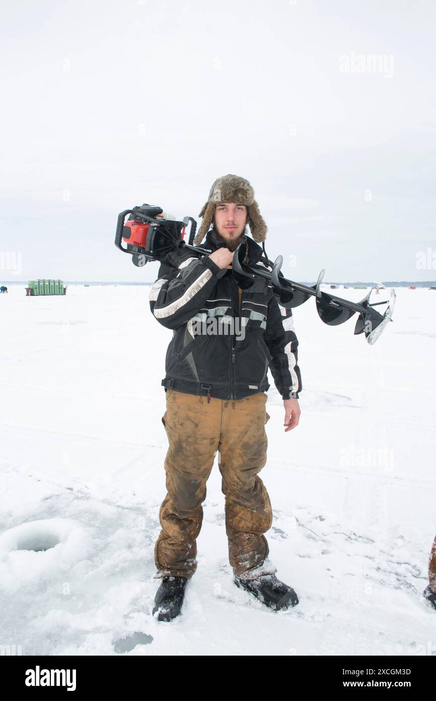 Un pescatore posa con la sua macchina perforatrice automatica per la pesca su ghiaccio al più grande torneo di pesca su ghiaccio del Minnesota di worldâ. Foto Stock