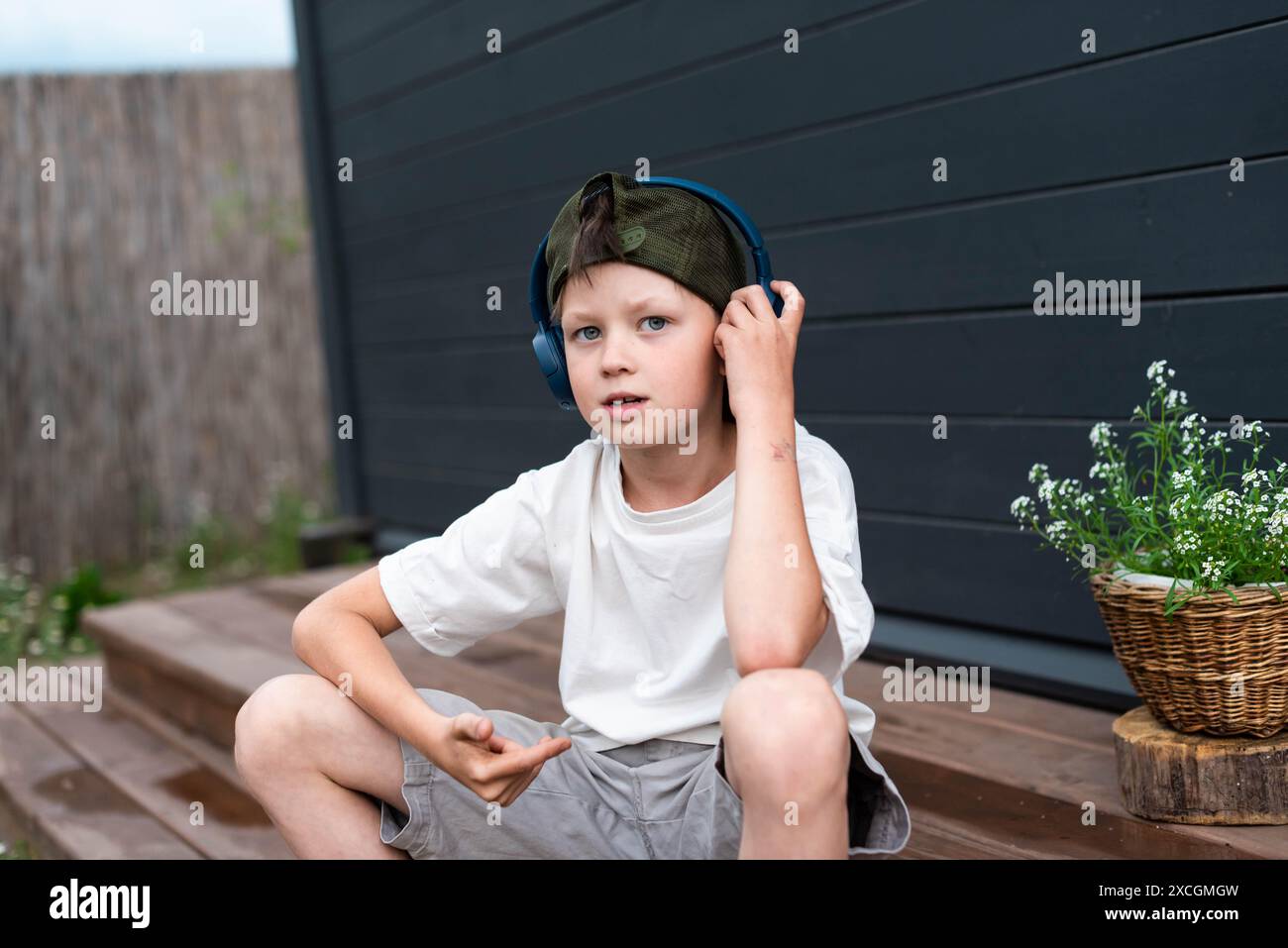 Simpatico ragazzo preadolescente con le cuffie che ascolta la musica su una terrazza in legno all'aperto Foto Stock