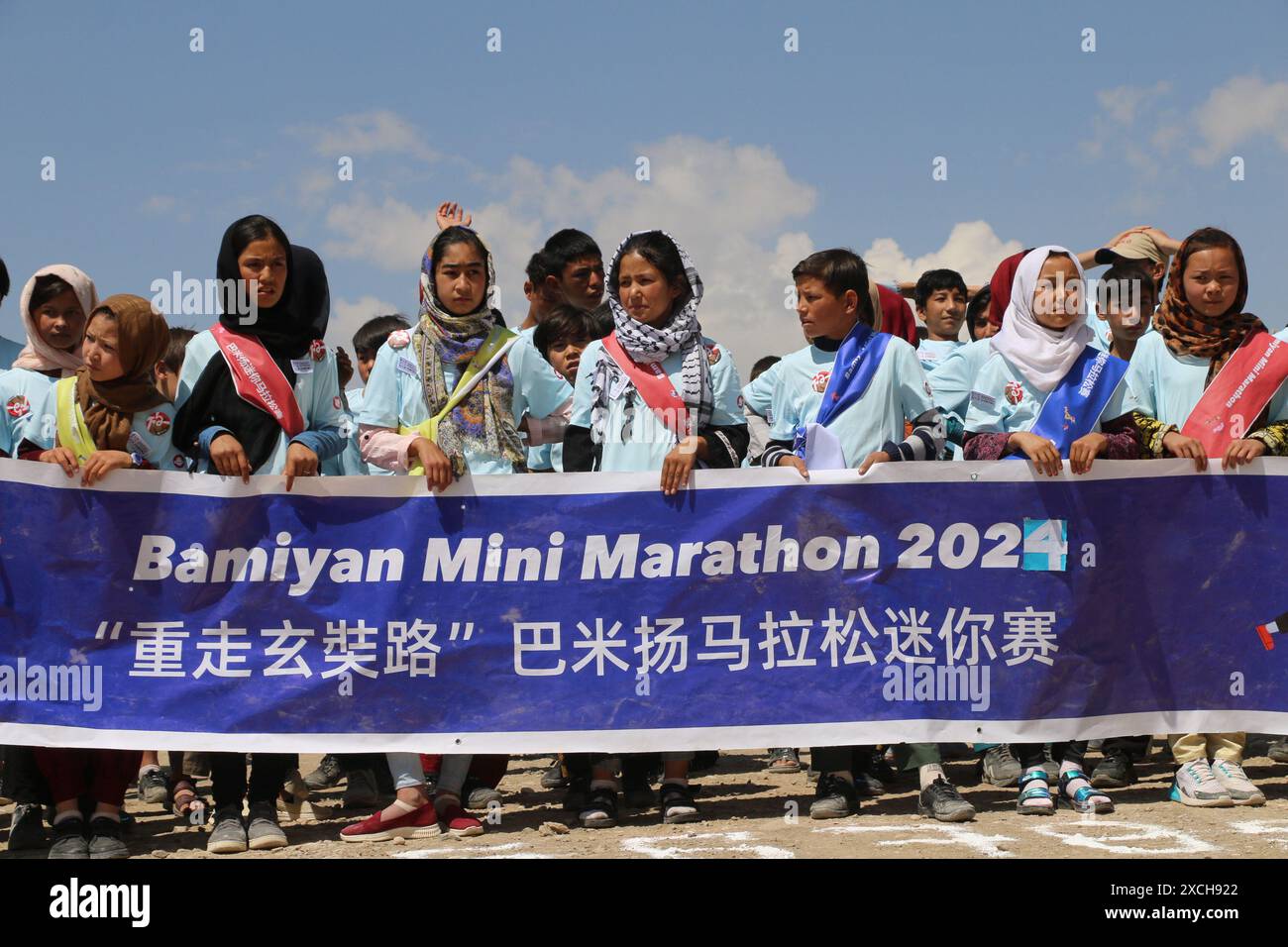 Bamiyan, Afghanistan. 15 giugno 2024. I bambini afghani tengono uno striscione per una mini-maratona mirata a sensibilizzare la popolazione locale sull'urgente necessità di proteggere le reliquie culturali nella provincia di Bamiyan, Afghanistan centrale, il 15 giugno 2024. ANDARE CON "Feature: I bambini afghani corrono per la protezione del patrimonio culturale in mini-maratona". Crediti: Ziaodin Azad/Xinhua/Alamy Live News Foto Stock