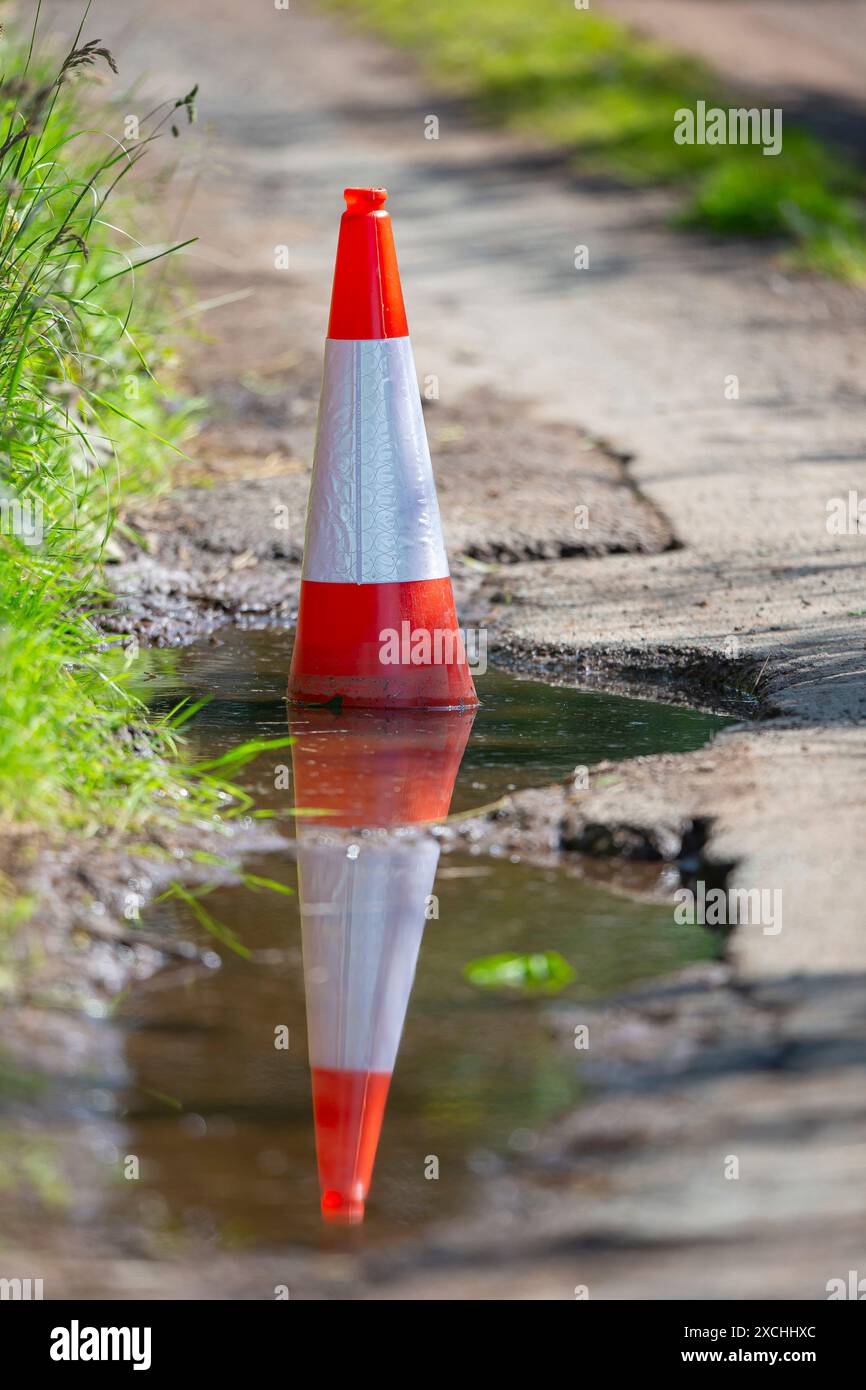 Buca profonda in una corsia di campagna piena d'acqua e segnata da un cono stradale. Foto Stock