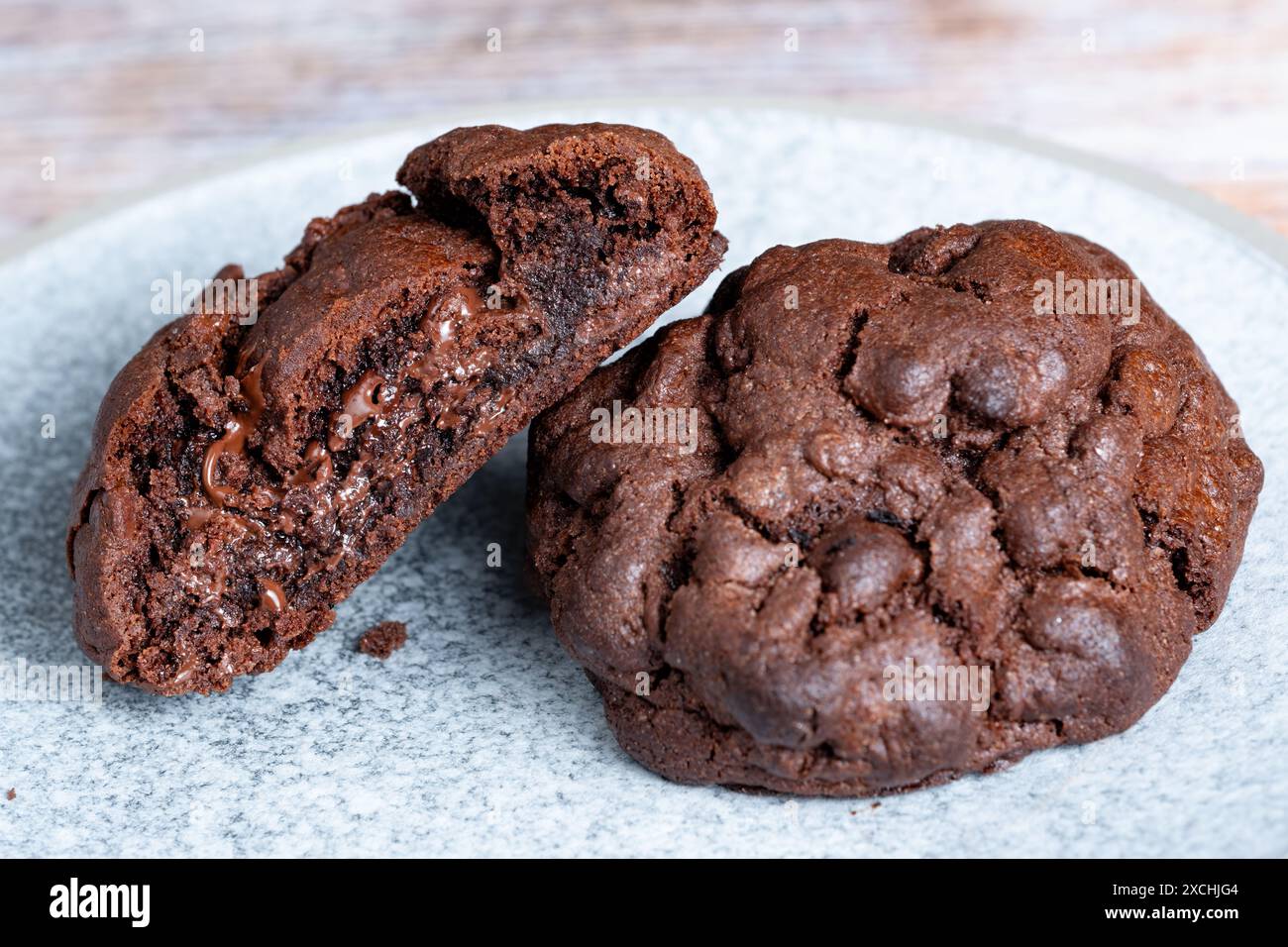Biscotti al cioccolato caldi appena sfornati in stile newyorkese che odorano il cioccolato. I biscotti sono serviti su un piatto con un taglio a metà per mostrare un ricco ripieno di cioccolato Foto Stock