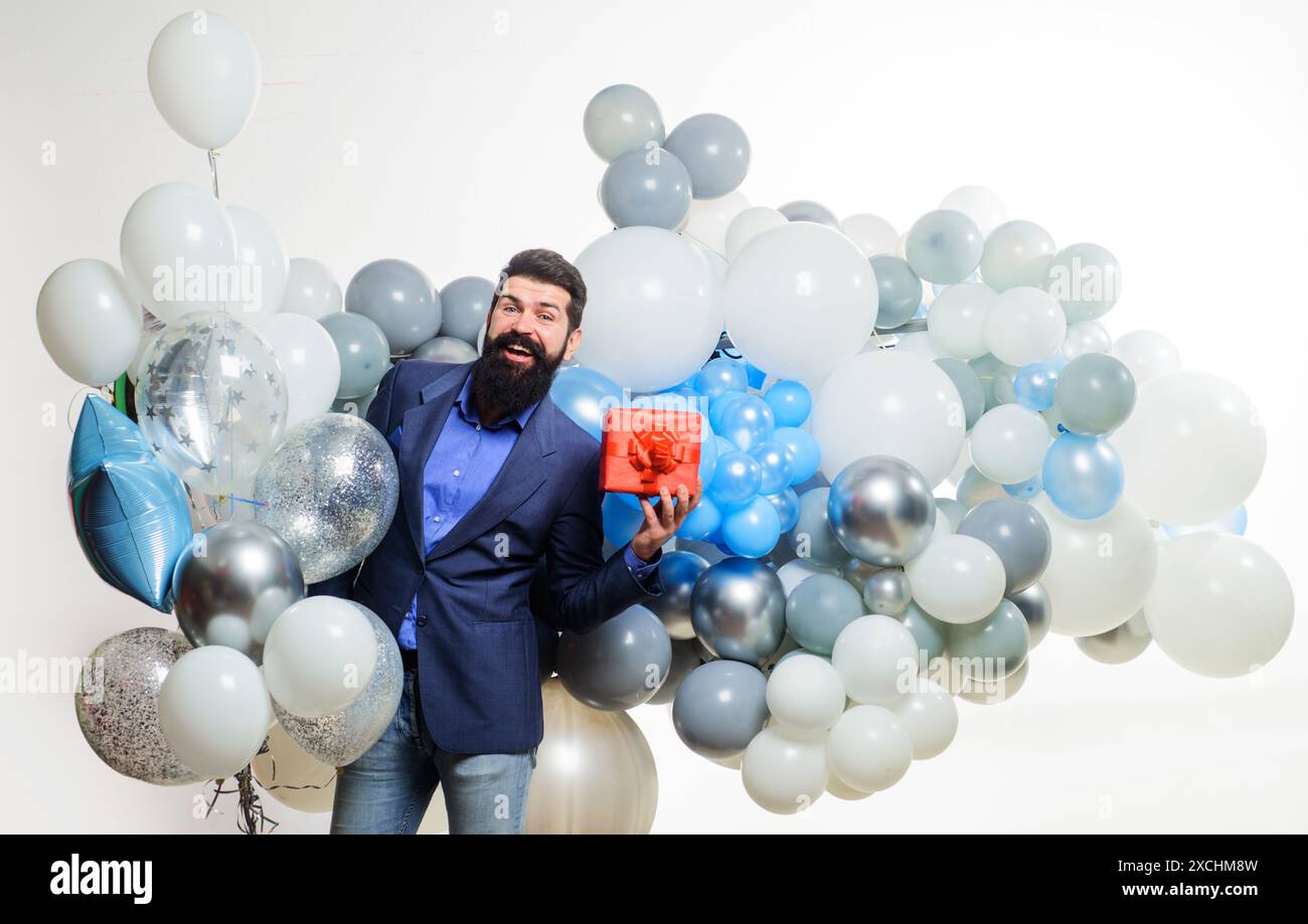 Regalo di compleanno. Uomo barbuto con palloncini all'elio e confezione regalo. Festività o feste di compleanno. Uomo d'affari felice con palloni gonfiabili Foto Stock