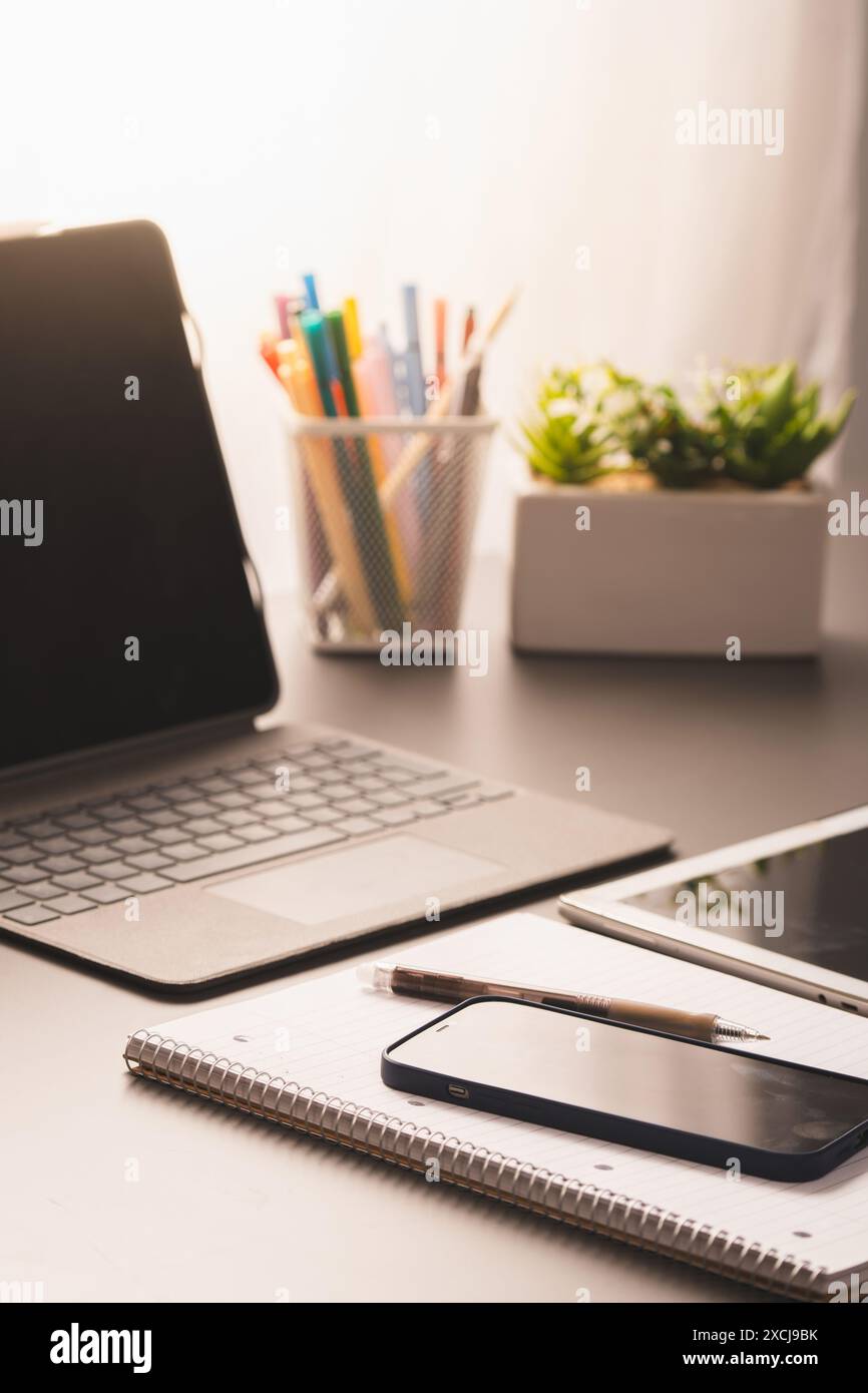 Una moderna scrivania da ufficio con laptop, notebook, smartphone, penna e forniture per ufficio. Configurazione perfetta per il lavoro remoto o lo studio - luminoso e luminoso Foto Stock