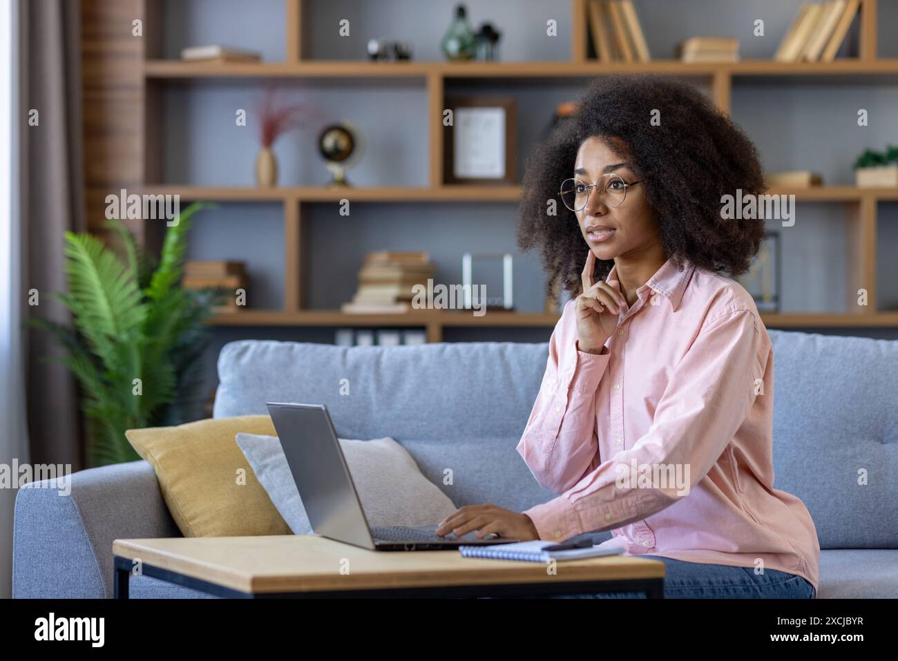 Giovane donna professionale che lavora da casa, utilizza un notebook, in un'attenta riflessione e concentrata nel salotto moderno. Foto Stock